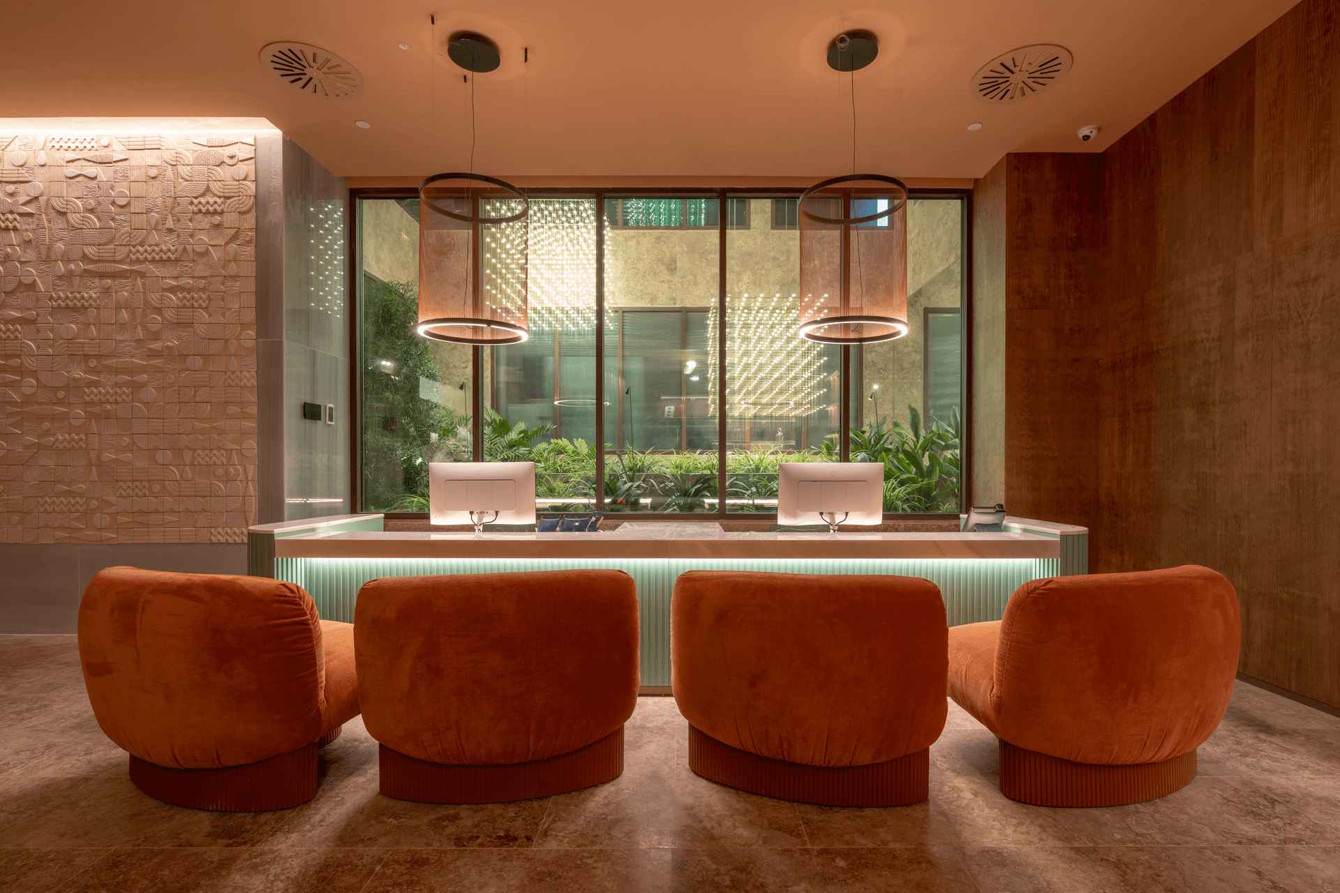 Mostrador de recepción del Hotel ME Málaga con grandes ventanales de aluminio STRUGAL, sillones naranjas y vista al patio interior